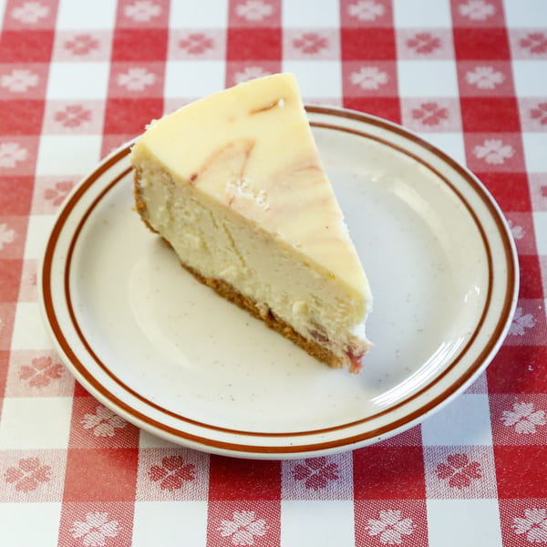 A slice of cheesecake with a graham cracker crust and a swirled topping on a white plate.