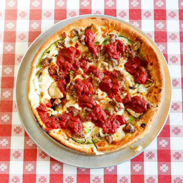 Deep dish pizza with chunky tomato sauce, sausage, mushrooms, and green peppers on a checkered tablecloth.