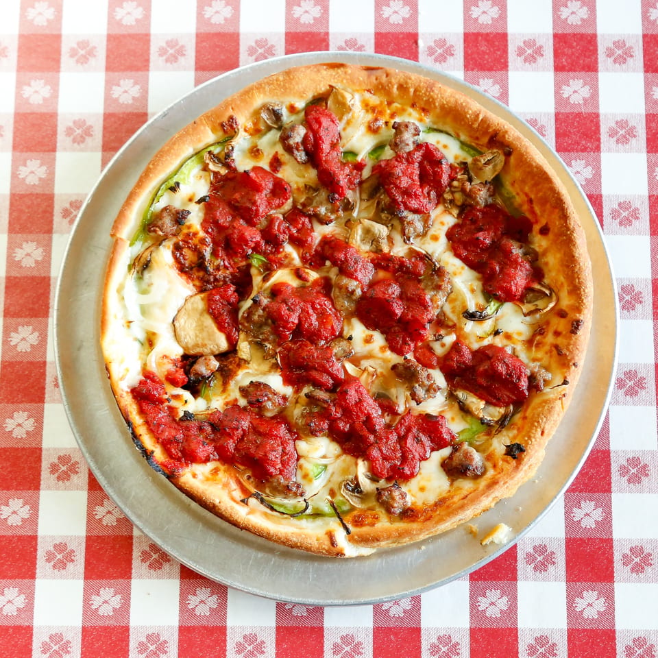 Deep dish pizza with chunky tomato sauce, sausage, mushrooms, and green peppers on a checkered tablecloth.