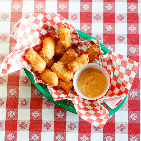 Golden-brown fried cheese curds in a green basket with red and white checkered paper, served with dipping sauce.