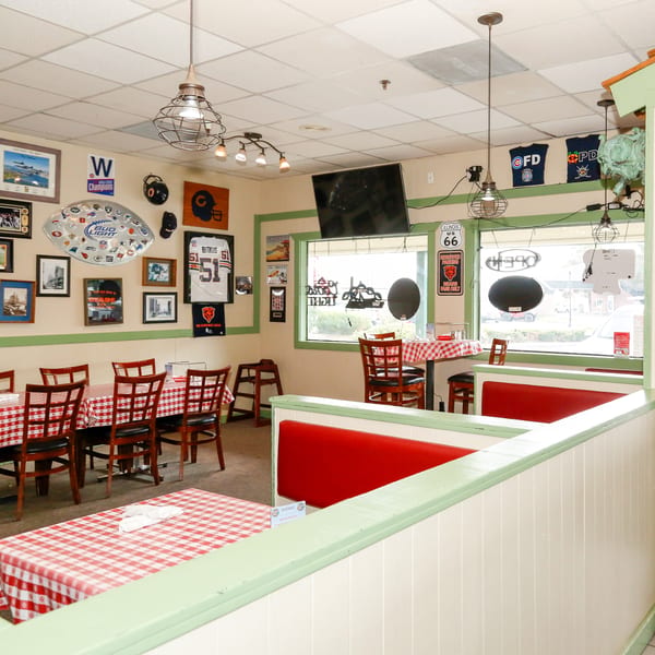 Interior of a casual restaurant with red and white checkered tablecloths, red booths, and sports memorabilia on the walls.