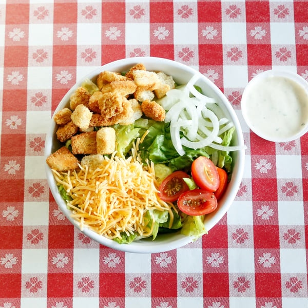 Overhead view of a garden salad with croutons, cheese, tomatoes, and onions on a red and white checkered tablecloth.